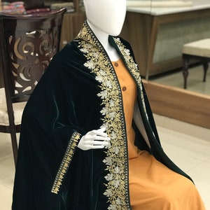 May include: A dark green velvet shawl with a white and gold embroidered border. The shawl is draped over a mannequin wearing a mustard yellow dress.