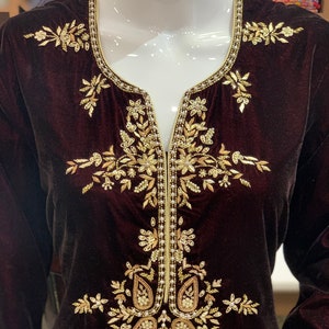 May include: A maroon velvet tunic with gold and pearl embroidery. The embroidery features a floral design with paisley shapes.