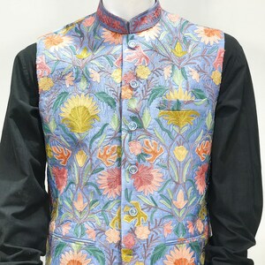 May include: A blue embroidered vest with a floral pattern in shades of pink, orange, yellow, and green. The vest has a mandarin collar and a button closure.