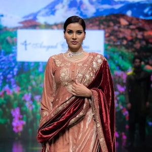 May include: A dusty rose velvet tunic and matching trousers set featuring intricate gold embroidery on the bodice and hem. The outfit is paired with a deep burgundy velvet shawl that has a wide gold embroidered border along the edges.