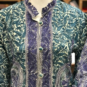 May include: A white jacket with a mandarin collar and intricate floral embroidery in shades of blue and purple.