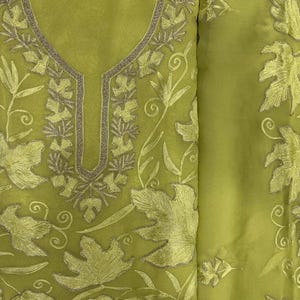 May include: A lime green fabric piece featuring intricate tonal leaf embroidery and a central neckline detail outlined in metallic gold thread. The sheer material displays a repeating pattern of foliage and swirling vine motifs across the surface.