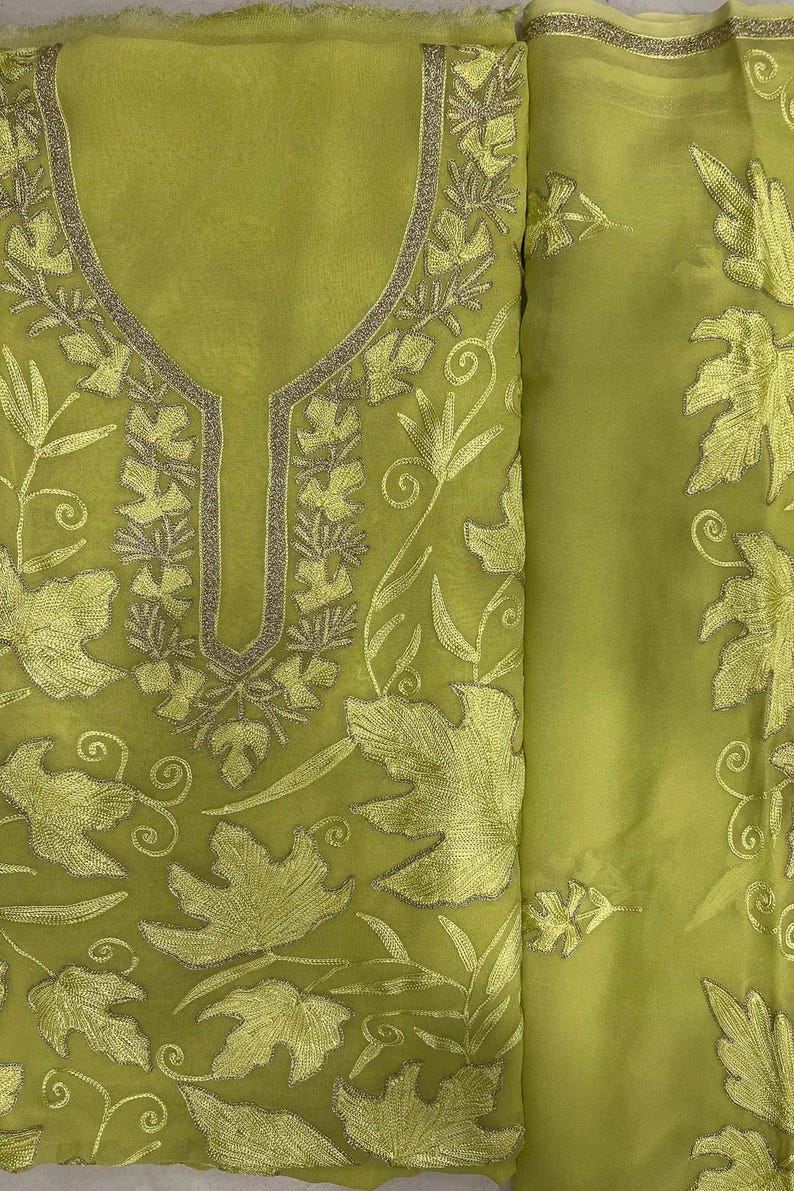 May include: A lime green fabric piece featuring intricate tonal leaf embroidery and a central neckline detail outlined in metallic gold thread. The sheer material displays a repeating pattern of foliage and swirling vine motifs across the surface.