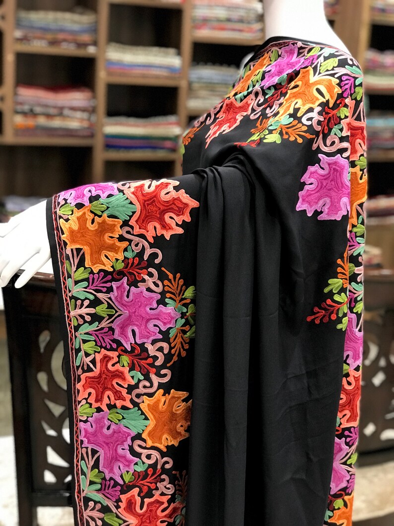 Peut inclure: Un ch&acirc;le noir avec une broderie florale color&eacute;e. La broderie pr&eacute;sente une vari&eacute;t&eacute; de couleurs, notamment le rose, l'orange, le vert et le rouge. Le ch&acirc;le est drap&eacute; sur un mannequin.