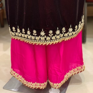 May include: A dark maroon velvet top with a pink skirt. Both pieces have gold embroidery and a maroon trim.
