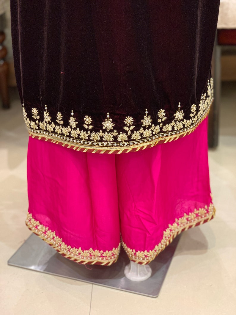May include: A dark maroon velvet top with a pink skirt. Both pieces have gold embroidery and a maroon trim.