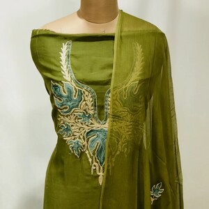 May include: A green cotton salwar kameez with a floral embroidered neckline and matching dupatta. The embroidery is in shades of green, gold, and white.