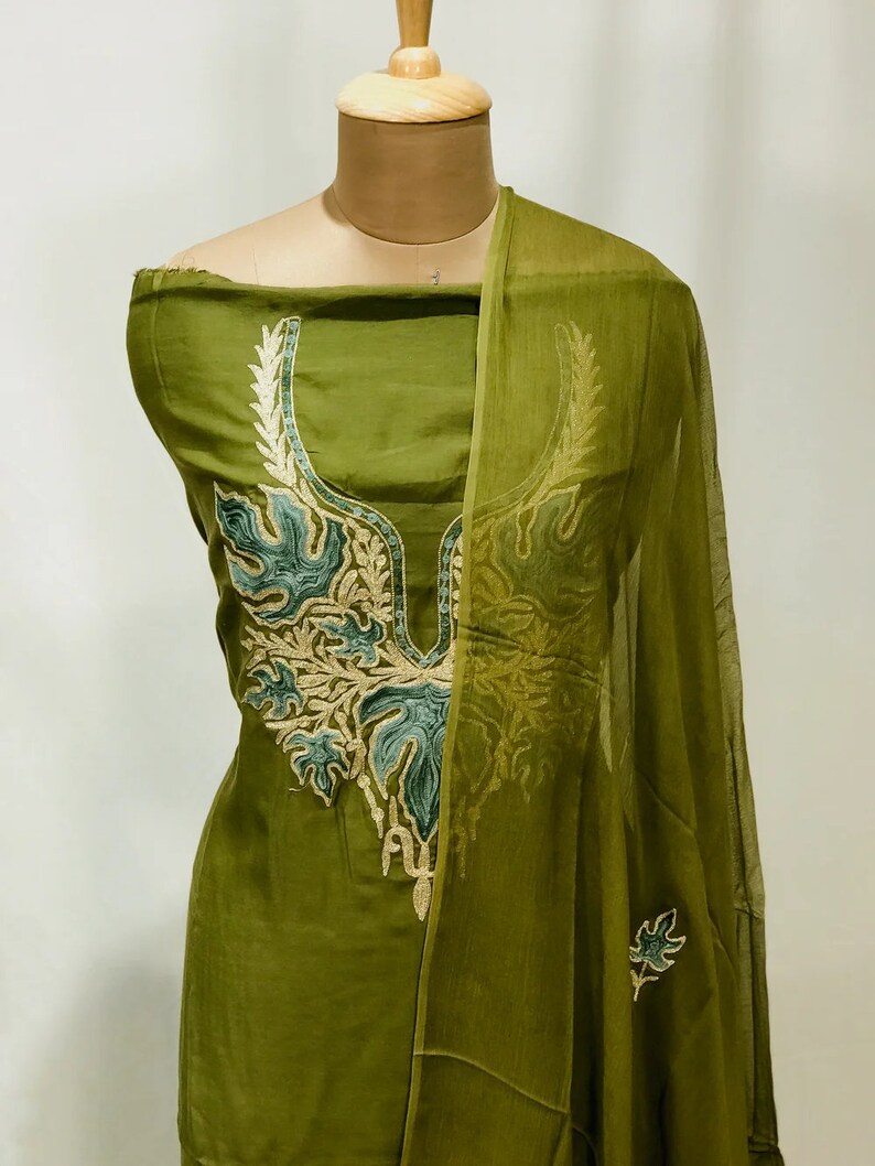 May include: A green cotton salwar kameez with a floral embroidered neckline and matching dupatta. The embroidery is in shades of green, gold, and white.
