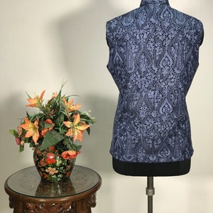 Puede incluir: Un chaleco azul sin mangas con un patr&oacute;n paisley negro. El chaleco est&aacute; en un maniqu&iacute; y tiene un cuello mandar&iacute;n.
