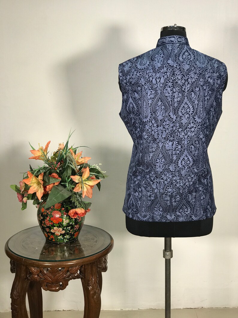 Puede incluir: Un chaleco azul sin mangas con un patr&oacute;n paisley negro. El chaleco est&aacute; en un maniqu&iacute; y tiene un cuello mandar&iacute;n.