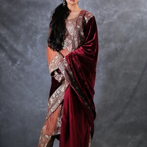 May include: A three-piece ensemble featuring a long-sleeved, copper-colored tunic and matching trousers, both adorned with intricate silver embroidery. A deep burgundy velvet shawl is draped over one shoulder, completing the formal outfit.