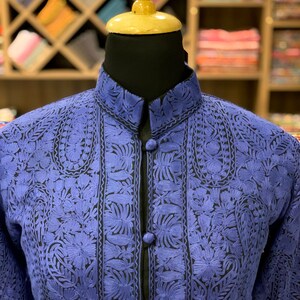 May include: A blue embroidered jacket with a mandarin collar and black trim. The jacket has a floral pattern and is fastened with buttons.