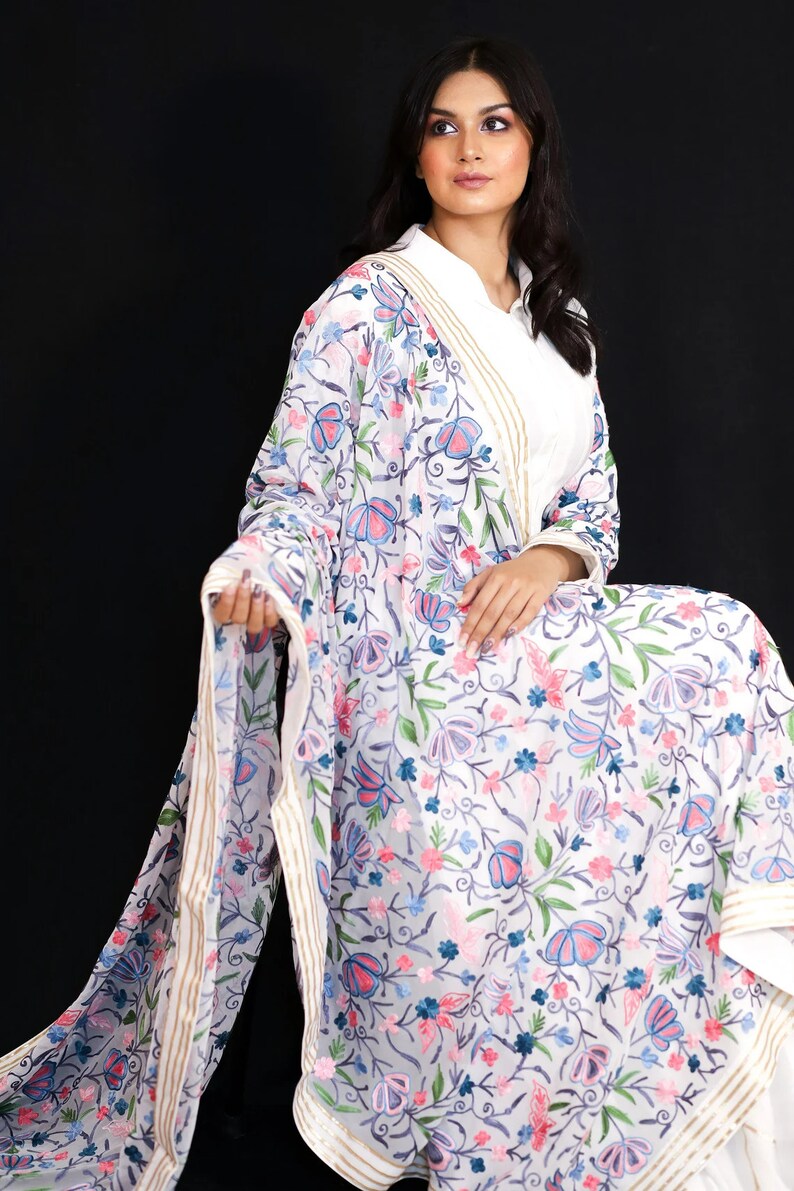 May include: White sheer shawl with a floral embroidery pattern in shades of pink, blue, and green. The shawl has a gold and white border.