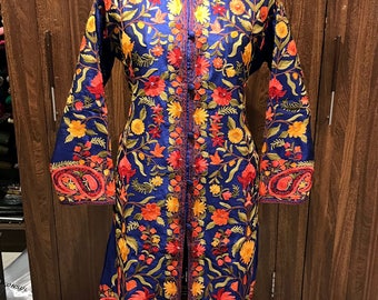 May include: A long blue embroidered tunic with a floral pattern in shades of orange, red, and yellow. The tunic has a mandarin collar and a button closure.