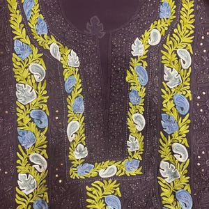 May include: A dark purple tunic featuring intricate embroidery along the neckline and front panel. The design includes vibrant lime green leafy vines interspersed with light blue and white paisley-shaped floral motifs and small metallic sequins.