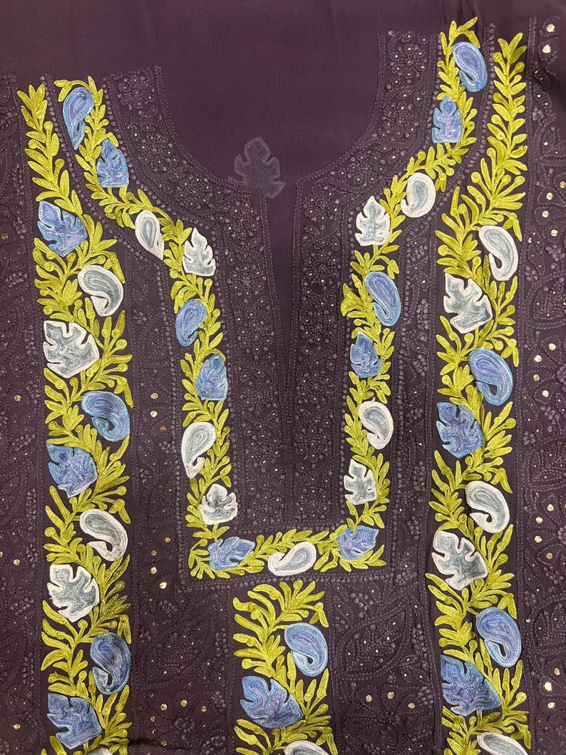May include: A dark purple tunic featuring intricate embroidery along the neckline and front panel. The design includes vibrant lime green leafy vines interspersed with light blue and white paisley-shaped floral motifs and small metallic sequins.