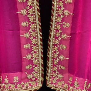 May include: A pink sheer scarf with a gold and white embroidered border. The border features a floral design with pearl accents.
