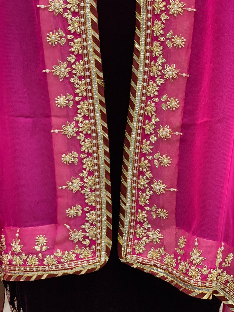 May include: A pink sheer scarf with a gold and white embroidered border. The border features a floral design with pearl accents.