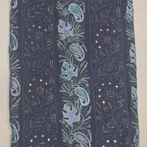May include: A dark grey fabric featuring vertical panels of intricate embroidery. The design includes alternating bands of floral patterns with small metallic sequins and central columns decorated with light blue and teal leaf and paisley motifs.