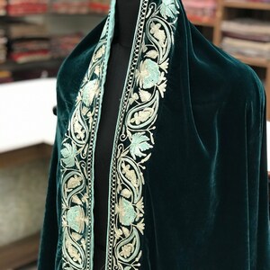 May include: A dark green velvet shawl with a light blue and white embroidered border. The embroidery features paisley and floral designs.