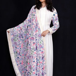 May include: A white long-sleeved dress with a floral embroidered dupatta. The dupatta has a white base with pink, blue, and green floral embroidery. The dress has a simple design with a collar and long sleeves.
