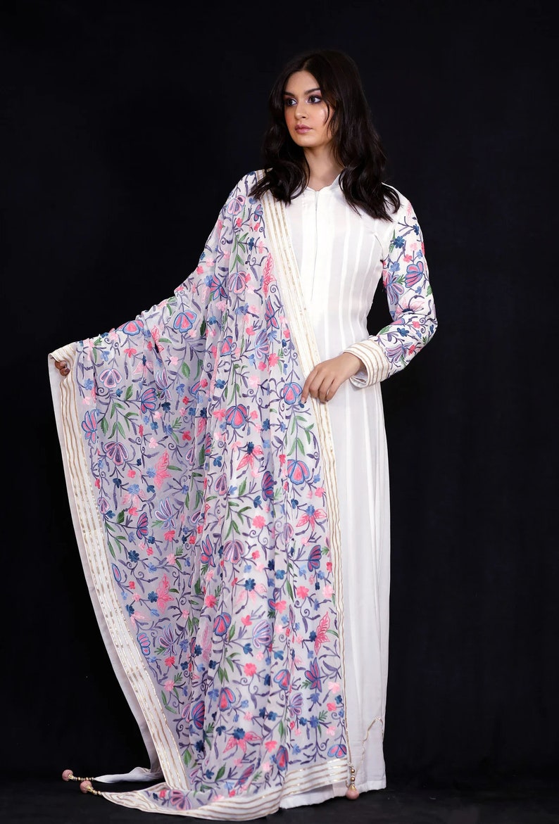 May include: A white long-sleeved dress with a floral embroidered dupatta. The dupatta has a white base with pink, blue, and green floral embroidery. The dress has a simple design with a collar and long sleeves.