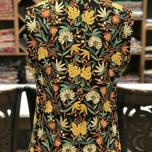 K&ouml;nnte beinhalten: Eine schwarze, &auml;rmellose Weste mit einem floralen Stickmuster in Gelb-, Gr&uuml;n-, Braun- und Rosat&ouml;nen.