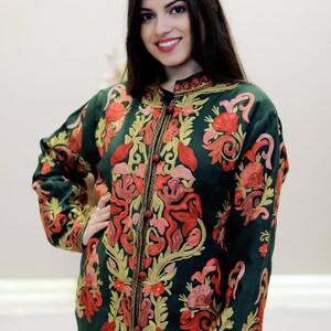 May include: A long, dark green embroidered jacket with a mandarin collar and floral patterns in shades of red, pink, and gold.