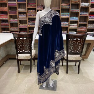 May include: A navy blue velvet shawl with a silver embroidered border. The shawl is draped over a mannequin in a retail store setting.