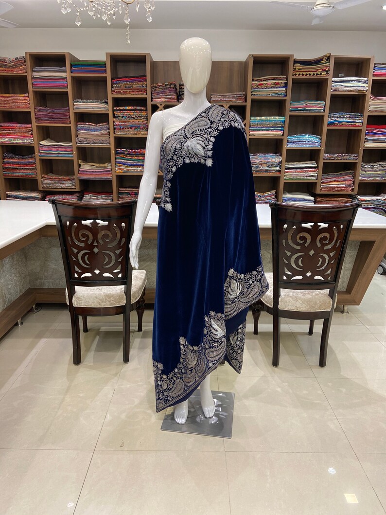 May include: A navy blue velvet shawl with a silver embroidered border. The shawl is draped over a mannequin in a retail store setting.