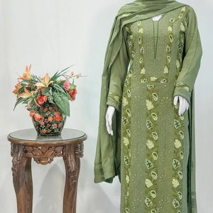 May include: An olive green three-piece outfit consisting of a long-sleeved tunic, trousers, and a matching dupatta. The tunic features intricate tonal embroidery, vertical panels with paisley and leaf motifs, and a notched neckline with subtle sequins.