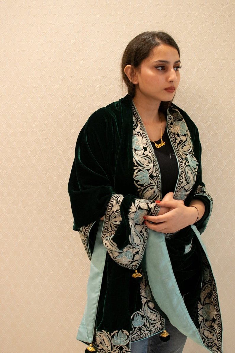 May include: A dark green velvet shawl with a light blue lining and intricate floral embroidery. The shawl has a fringed edge and gold tassels.