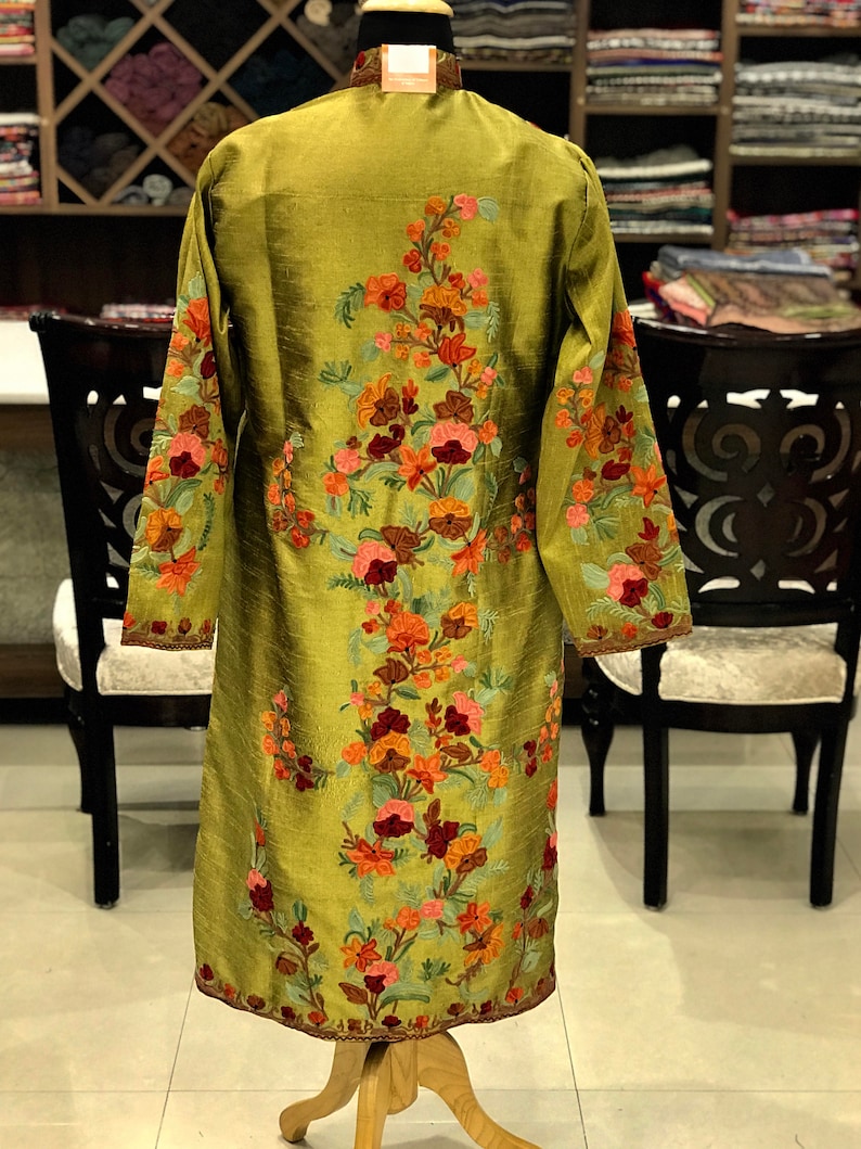 May include: A long-sleeved olive green tunic featuring intricate floral embroidery in shades of orange, pink, and deep red. The garment has a high collar and a straight silhouette, with the floral pattern extending from the neckline to the hem.