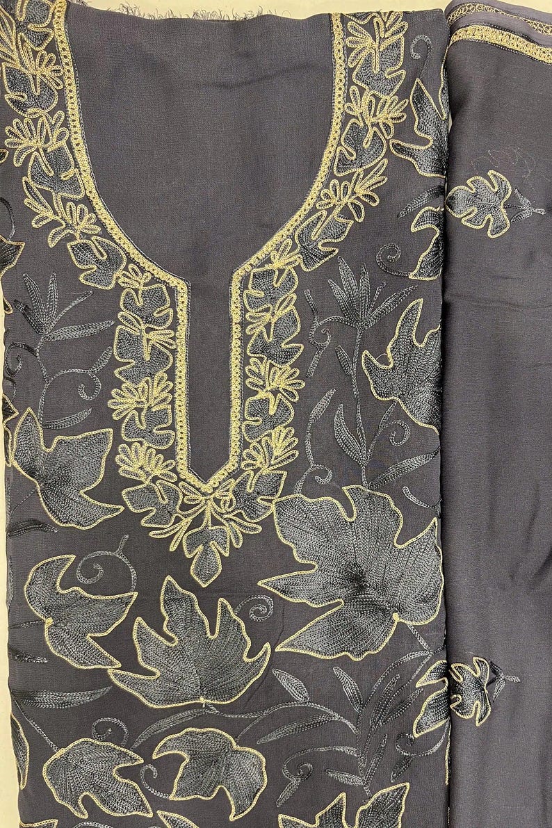 May include: A dark charcoal gray fabric garment featuring intricate embroidery of large leaves and vines. The embroidery is executed in a combination of black thread and metallic gold thread, which outlines the leaf patterns and the neckline.