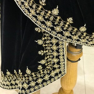 Puede incluir: Tela de terciopelo negro con bordado de cuentas doradas y blancas. El bordado presenta un dise&ntilde;o floral.