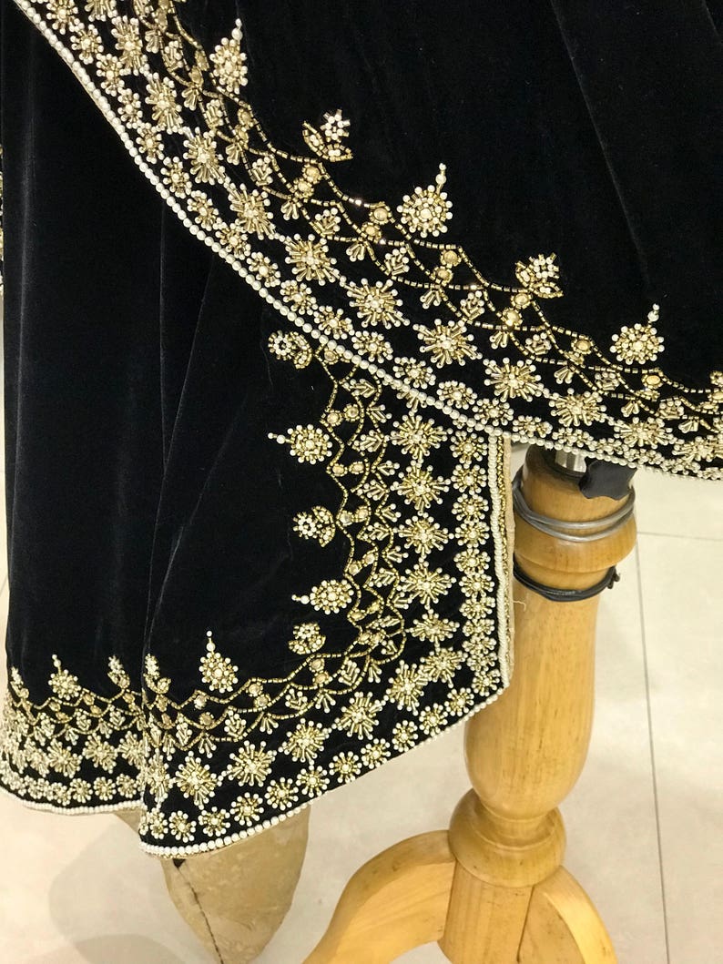 Puede incluir: Tela de terciopelo negro con bordado de cuentas doradas y blancas. El bordado presenta un dise&ntilde;o floral.
