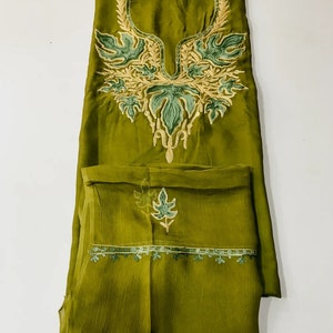 May include: A green salwar kameez with intricate embroidery in shades of green and gold. The neckline features a floral design, and the bottom hem has a delicate border.