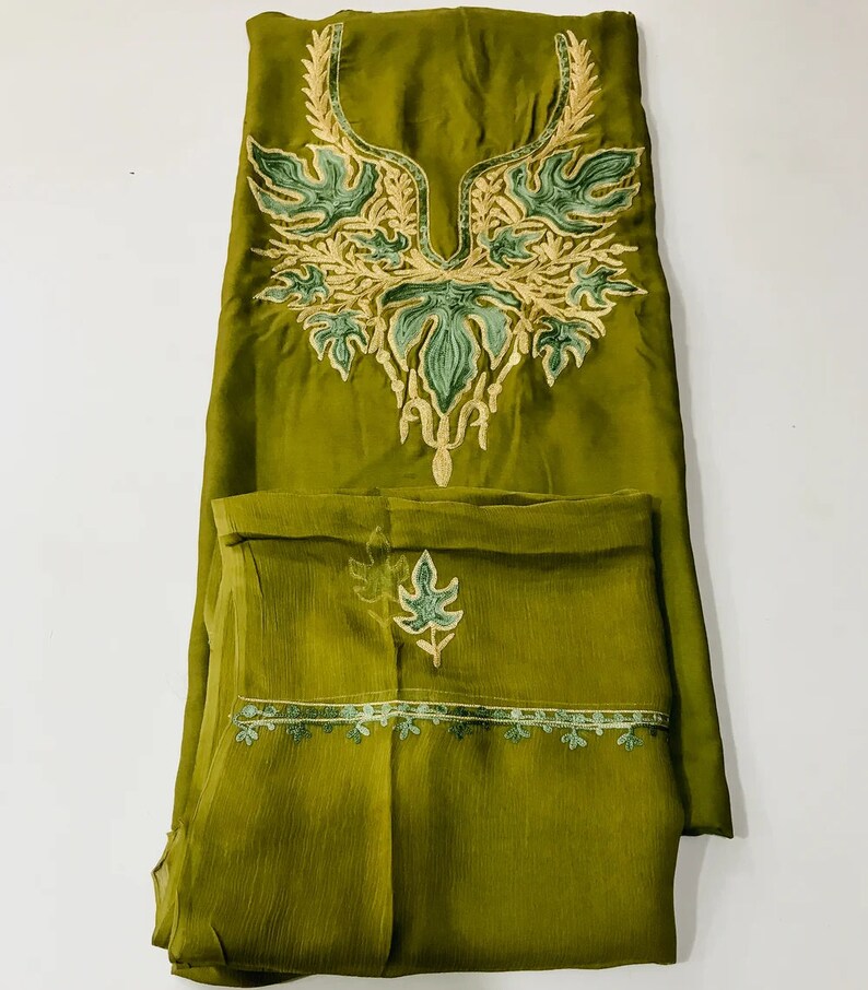 May include: A green salwar kameez with intricate embroidery in shades of green and gold. The neckline features a floral design, and the bottom hem has a delicate border.
