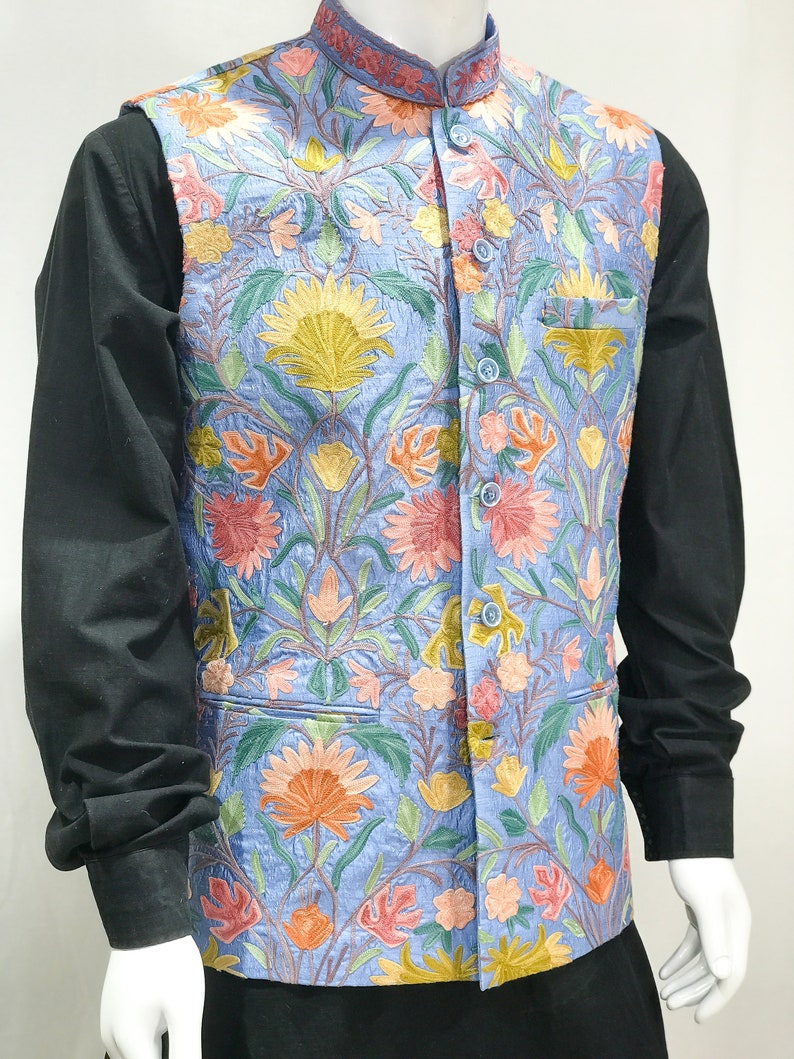 May include: A light blue vest with a floral embroidery pattern. The vest has a mandarin collar and a button closure.