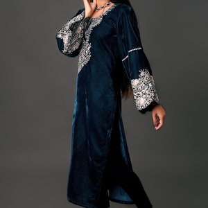 May include: A teal velvet tunic with intricate embroidery on the sleeves and neckline. The long-sleeved tunic features a high slit and is paired with black pants and heels. The outfit is elegant and suitable for special occasions.