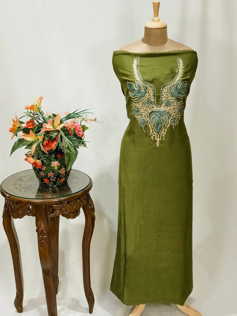 May include: A green fabric with a decorative embroidered neckline. The embroidery is in shades of green and gold.