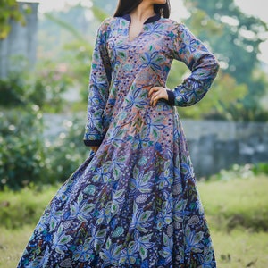 May include: A long-sleeved, floor-length dress with a floral print in shades of blue, green, and pink. The dress has a high neckline and a fitted bodice. The skirt is full and flowing.