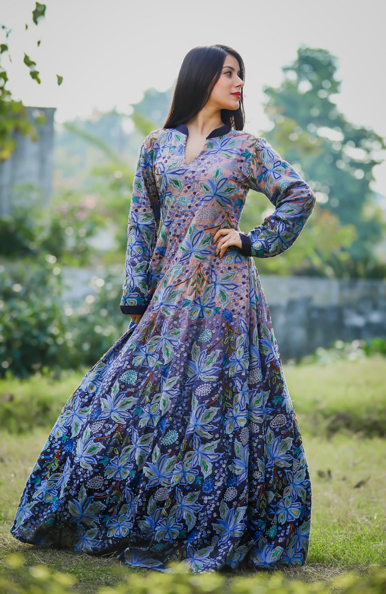 May include: A long-sleeved, floor-length dress with a floral print in shades of blue, green, and pink. The dress has a high neckline and a fitted bodice. The skirt is full and flowing.