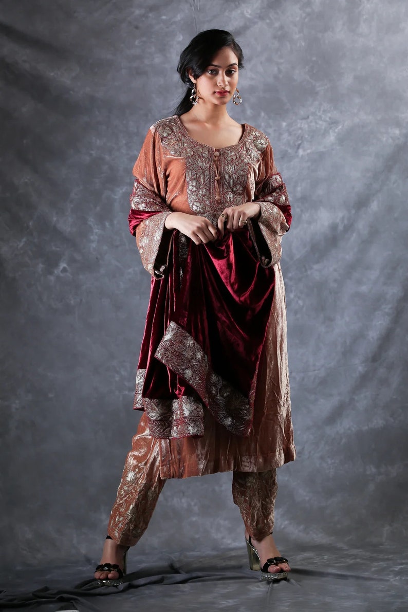 May include: A copper-colored velvet tunic and matching trousers featuring intricate silver embroidery around the neckline and cuffs, paired with a deep burgundy velvet shawl that has a wide silver embroidered border along the edges.