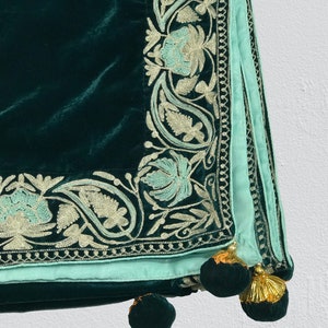 May include: A dark green velvet throw blanket with a light blue and silver embroidered border. The blanket has tassels on the corners.