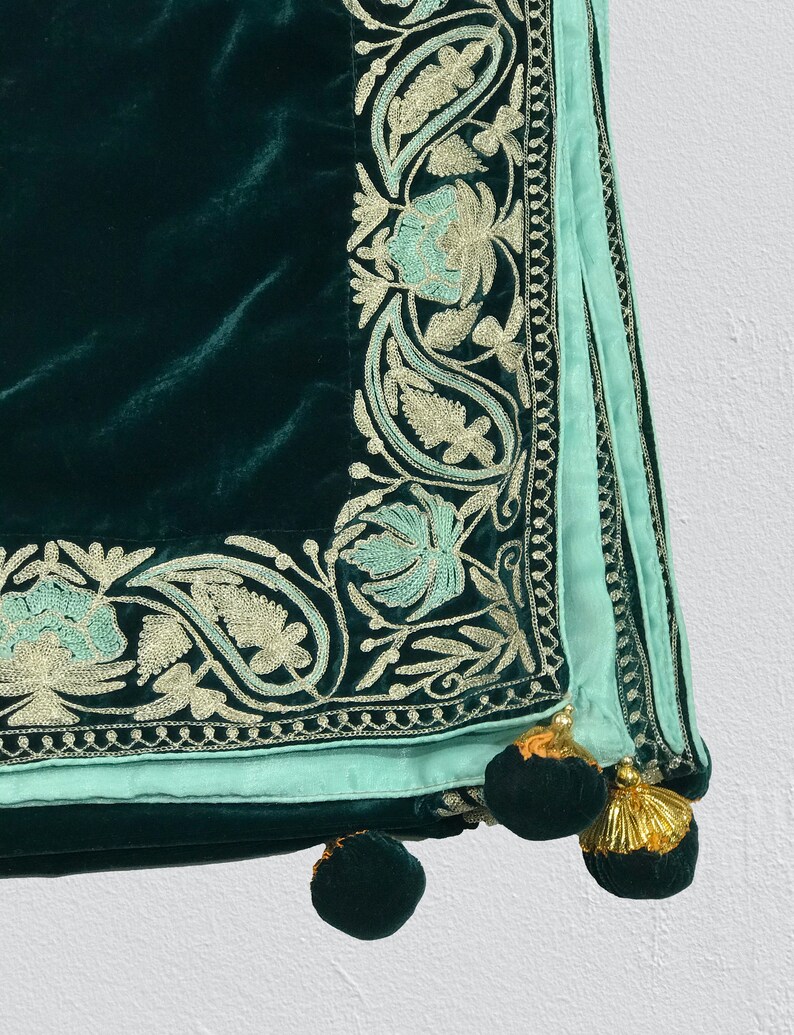 May include: A dark green velvet throw blanket with a light blue and silver embroidered border. The blanket has tassels on the corners.
