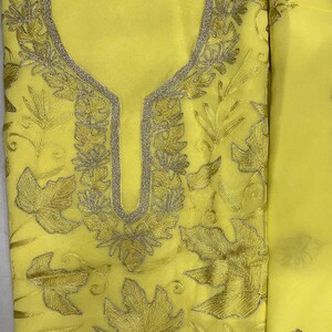 May include: A bright yellow fabric garment featuring intricate embroidery in a matching yellow thread. The design includes detailed leaf motifs scattered across the surface and a prominent, U-shaped neckline bordered by a metallic silver trim.