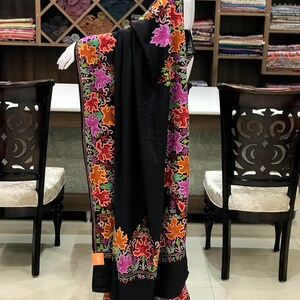 Peut inclure: Un ch&acirc;le noir avec des broderies florales color&eacute;es. Le ch&acirc;le est drap&eacute; sur un mannequin et a un design long et fluide.