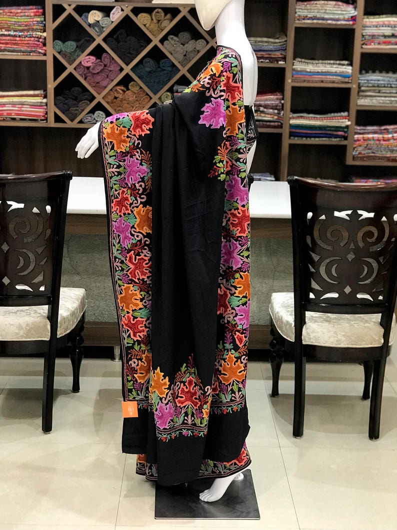 Peut inclure: Un ch&acirc;le noir avec des broderies florales color&eacute;es. Le ch&acirc;le est drap&eacute; sur un mannequin et a un design long et fluide.