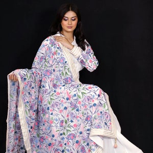 May include: A white embroidered dupatta with a floral pattern in shades of pink, blue, and green. The dupatta has a gold and white border.
